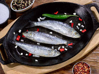 Uncooked Whole Sardines in a black skillet with peppers