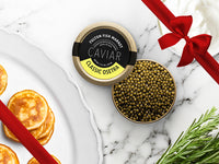 Classic Osetra Caviar Tin Opened on Marble Surface with Creme Fraiche and Blinis with Gift Bow Graphic on Top Right