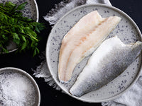 Branzino Fillets on Plate Next to Herbs and Seasonings