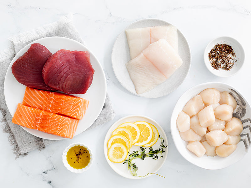 Tuna Steaks, Sea Scallops, Atlantic Halibut Portions, and Atlantic Salmon Portions on Plates on Marble Surface