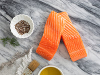King Salmon Portions on Marble Surface with Olive Oil and Cooking Brush Next to it with Seasonings and Herbs