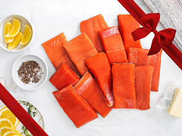 Wild Alaska Sockeye Salmon and Coho Salmon Portions on Kitchen Counter with Lemon Wedges, Seasoning, and Butter with Gift Bow Graphic on Top Right