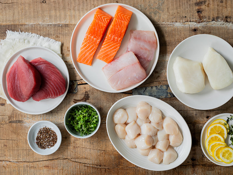 Sea Scallops, Atlantic Halibut Portions, Red Snapper Portions, Atlantic Salmon Portions, and Ahi Tuna Steaks on Plates on Wood Table