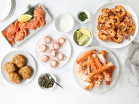 Smoked salmon, crab cakes, bacon-wrapped scallops, center cut crab legs, grilled shrimp with limes and seasonings on a marble background