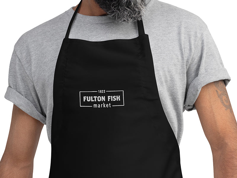 Person wearing a black apron with a white embroidered Fulton Fish Market Logo