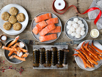 Atlantic Salmon Portions, Sea Scallops, King Crab Legs, Cold Water Lobster Tails, and Crab Cakes on Wood Table with Gift Ribbon Unraveling
