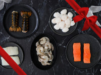 Lobster Tails, Scallops, Shrimp, Halibut, and Salmon on Plates on Dark Marble Table with Gift Ribbon