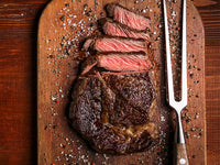 Cooked Japanese A5 Wagyu Ribeye Sliced on Wood Cutting Board with cooking fork and spices