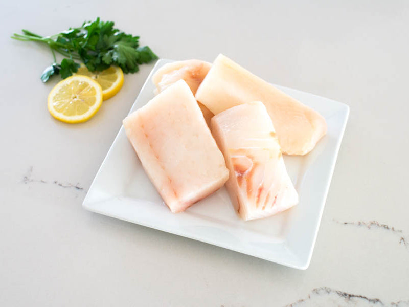 Wild Alaska Halibut Portions on White Plate with Lemons and Herbs