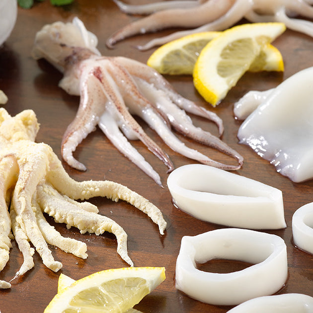 Whole Squid and Squid Rings and Tubes on Wooden Surface with Lemon and Herbs