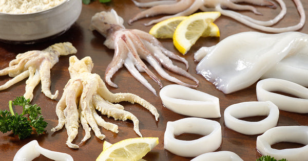 Whole Squid and Squid Rings and Tubes on Wooden Surface with Lemon and Herbs