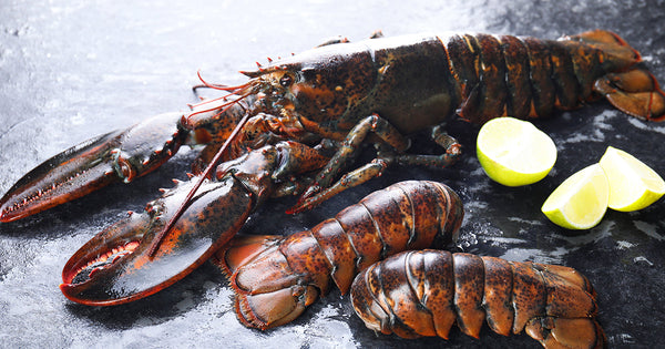 Whole Lobster and Lobster Tails on Dark Surface with Lemon Wedges