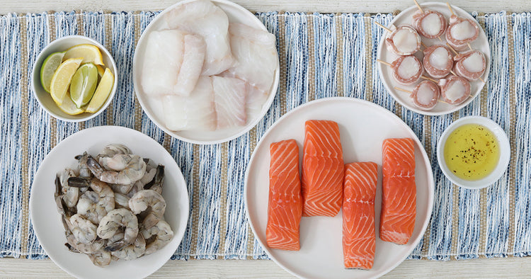 Assortment of Seafood including Salmon, Shrimp, Bacon-Wrapped Scallops, and Atlantic Cod on White Plates on a Striped Table Cloth