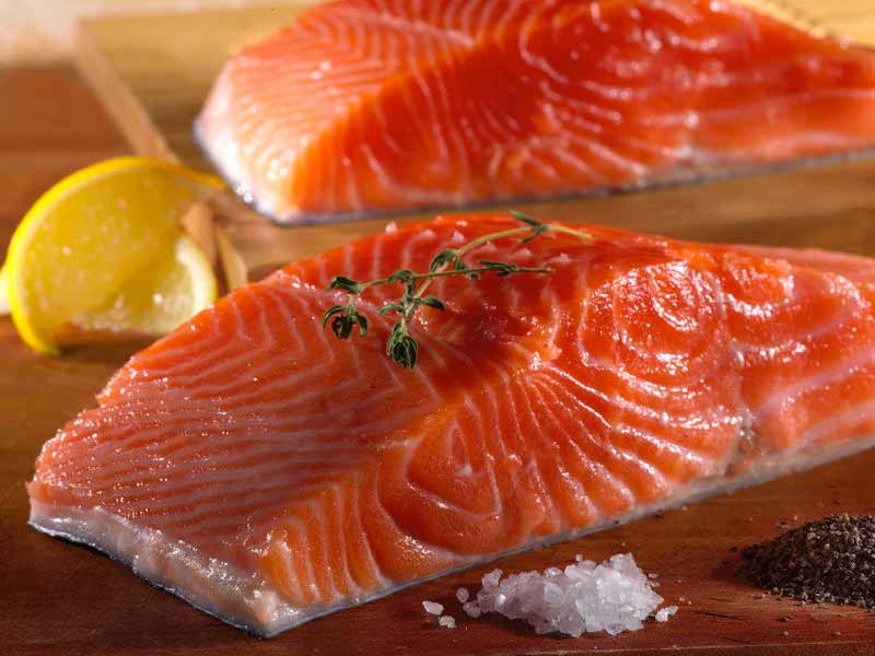 King Salmon Portions on Wood Cutting Board with Salt & Pepper and Lemon Wedges