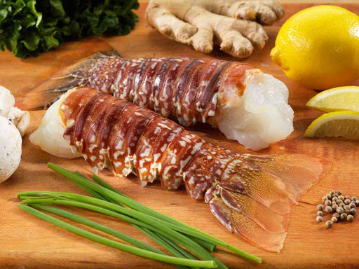 Two Wild South African Cold Water Lobster Tails on Wood Cutting Board with Chives, Lemon, Ginger and Peppercorns