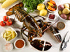 Extra Large Live Cold Water Lobster On White Table Surrounded by Herbs, Spices, Tomatoes, Potatoes, and Lemons