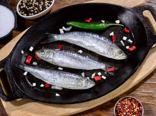 Uncooked Whole Sardines in a black skillet with peppers
