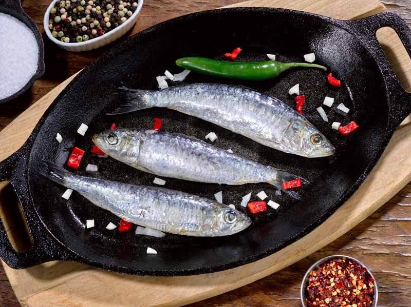 Uncooked Whole Sardines in a black skillet with peppers