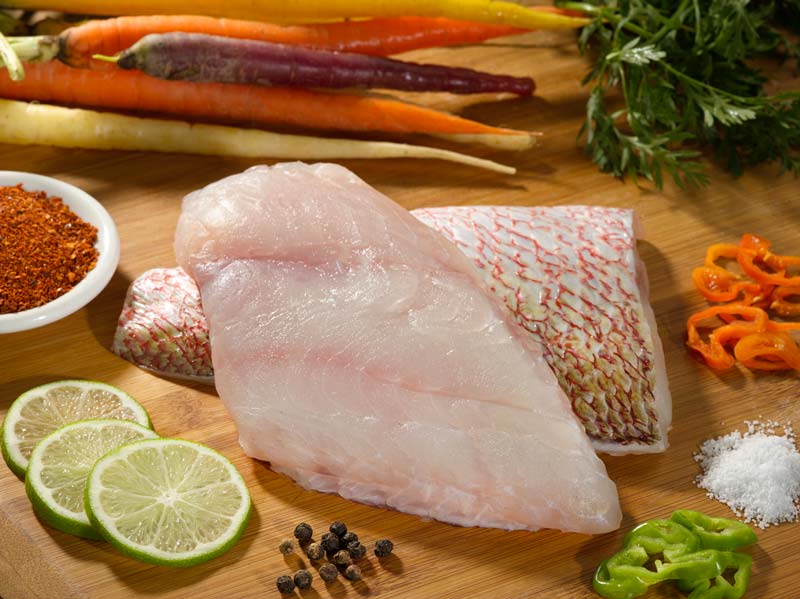 American Red Snapper Portions on Wooden Surface with Peppers, Carrots, Limes, Herbs and Spices