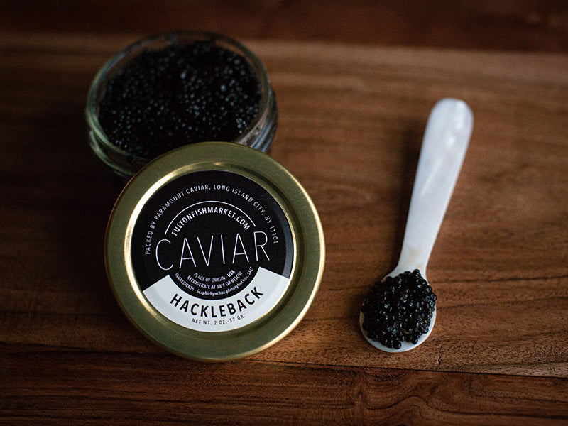 Hackleback Caviar Jar on Wooden Surface with Caviar on Top of Mother of Pearl Spoon