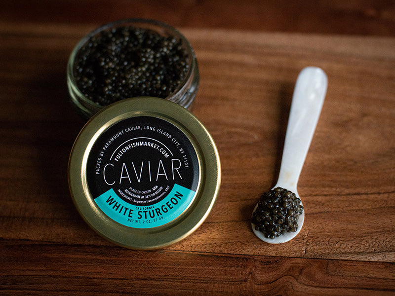 California White Sturgeon Caviar Open Jar with Caviar on Mother of Pearl Spoon on Wooden Surface