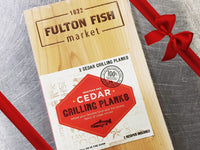 Western Red Cedar Grilling Plank on Steel Surface with Gift Bow Graphic on Top Right
