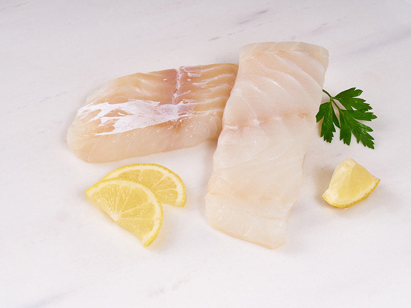 Wild Atlantic Cod Center Cut Portions on Light Surface with Lemon and Herbs