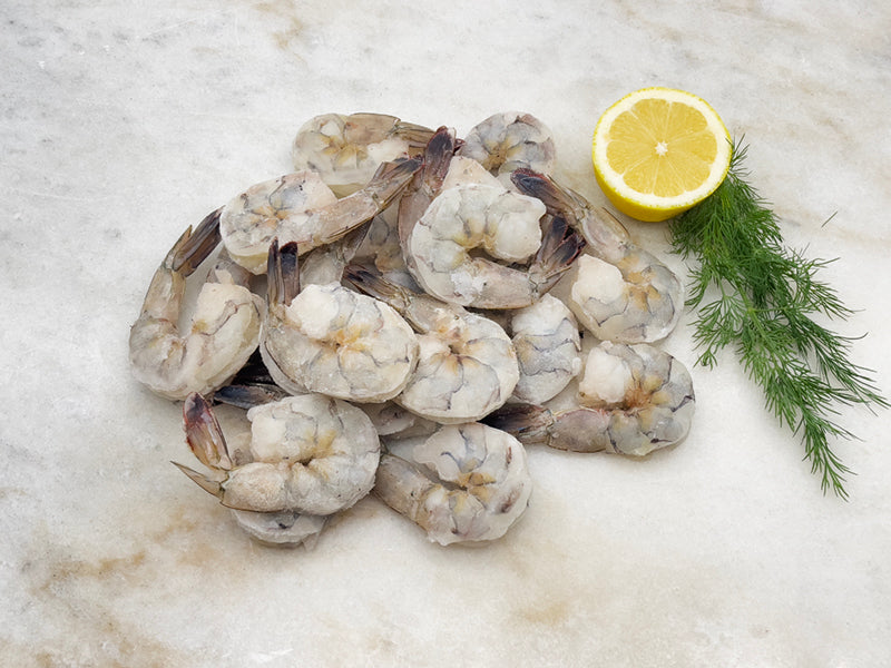 Wild Colossal Peeled & Deveined Blue Shrimp in a Pile on Marble Surface with Lemon and Herbs