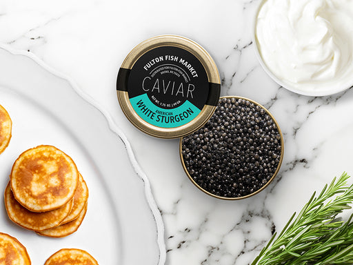 American White Sturgeon Caviar Tin Opened on Marble Surface with Creme Fraiche and Blinis