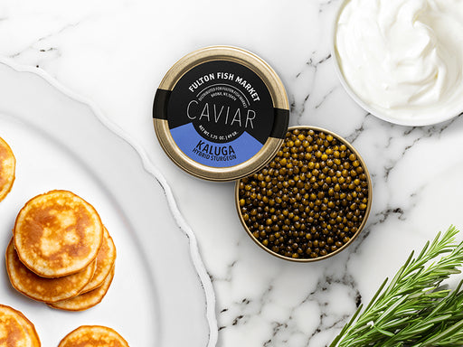 Kaluga Hybrid Strugeon Caviar Tin Opened on Marble Surface with Creme Fraiche and Blinis