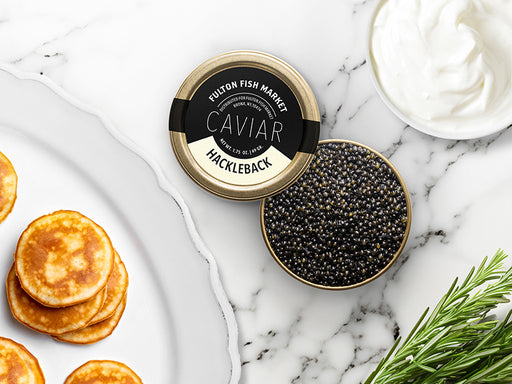 Hackleback Caviar Tin Opened on Marble Surface with Creme Fraiche and Blinis