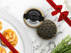 Paddlefish Caviar Tin Opened on Marble Surface with Creme Fraiche and Blinis with Gift Bow Graphic on Top Right