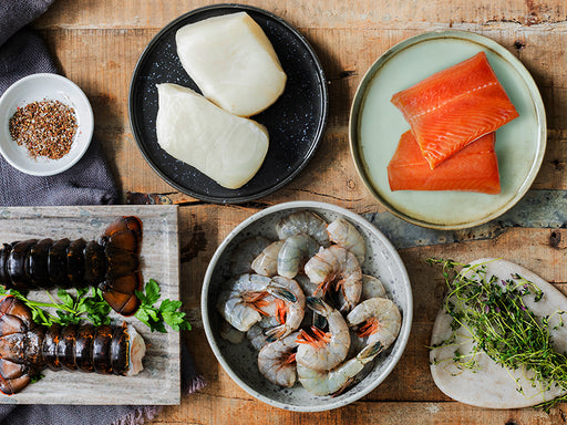 Lobster Tails, Chilean Sea Bass Portions, Wild Alaska Sockeye Salmon Portions, and Wild Blue Shrimp on Table with Seasonings and Herbs