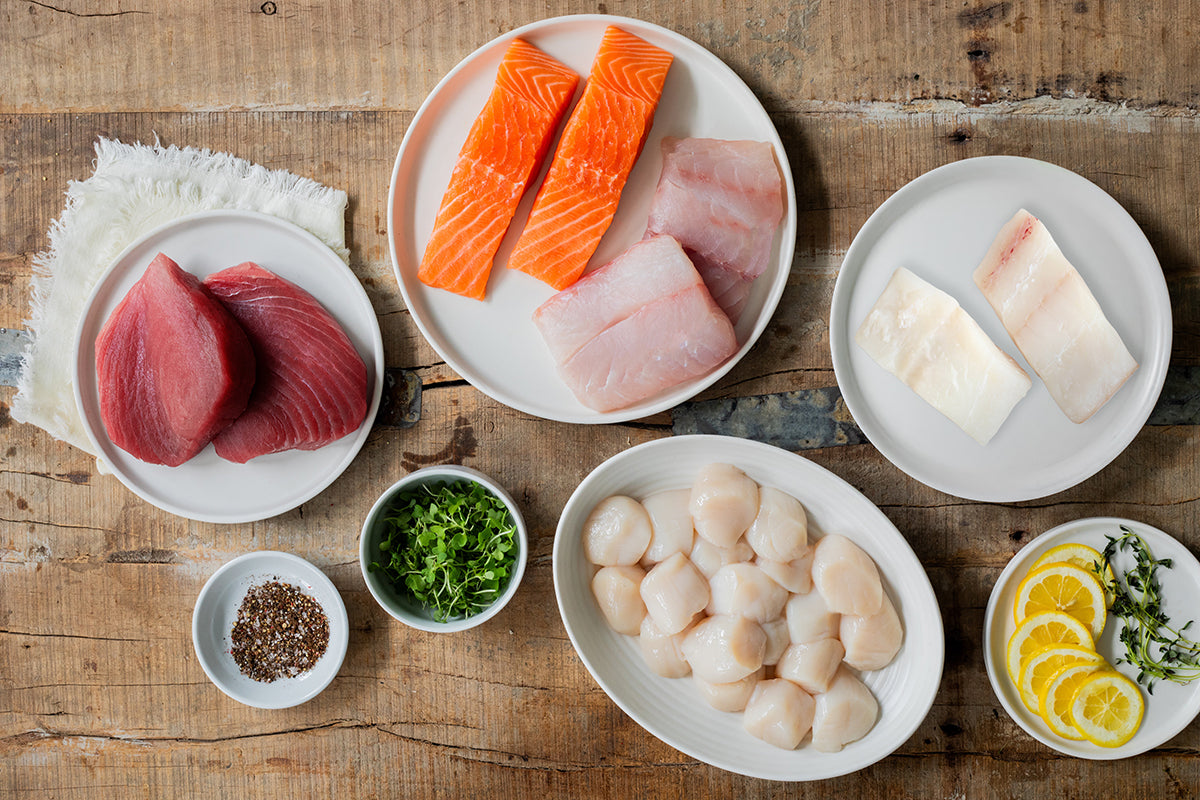 Sea Scallops, Atlantic Halibut Portions, Red Snapper Portions, Atlantic Salmon Portions, and Ahi Tuna Steaks on Plates on Wood Table