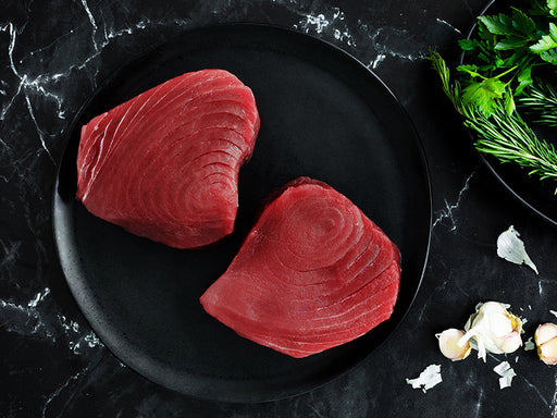 Ahi Tuna Steaks on Plate on Dark Marble Surface with Garlic Cloves and Herbs