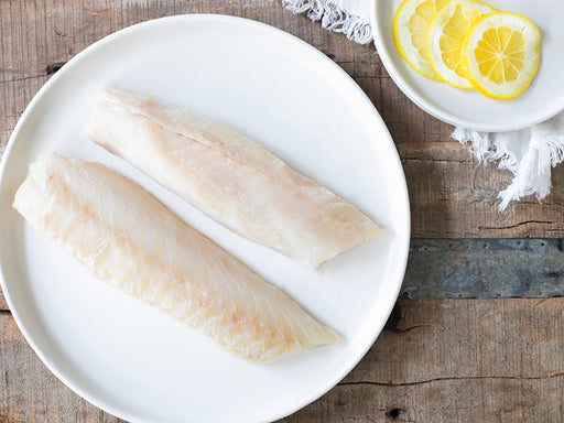 Atlantic Cod Portions on Plate On Wood Table with Lemon Slices