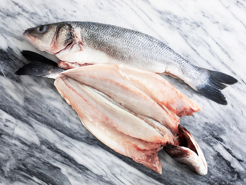 Pair of Butterflied Branzino on Marble Surface with One Opened to Show How It Is Cut