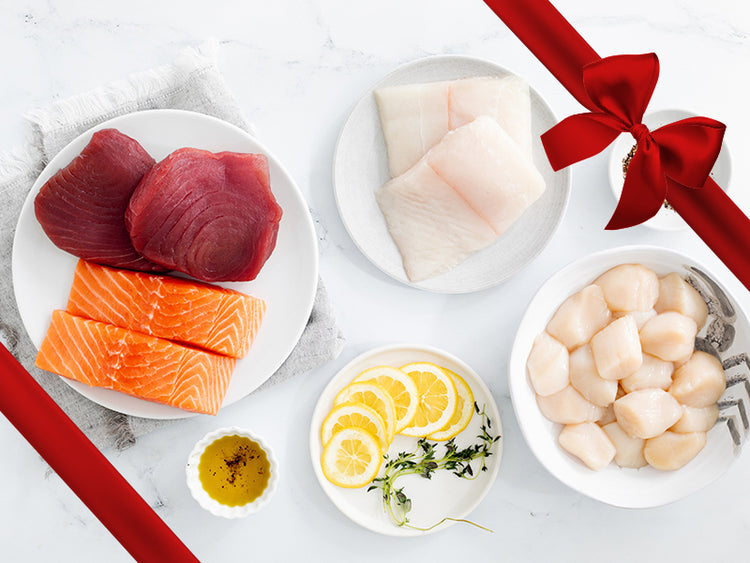 Tuna Steaks, Sea Scallops, Atlantic Halibut Portions, and Atlantic Salmon Portions on Plates on Marble Surface with Gift Bow Graphic on Top Right