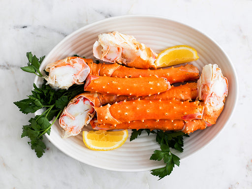 Golden King Crab Legs in White Serving Dish with Lemon Wedges and Parsley