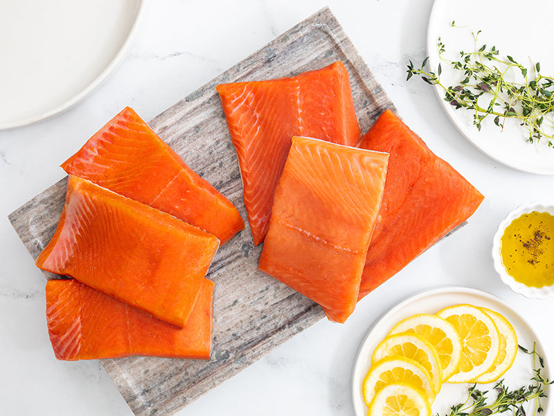Wild Alaska Sockeye Salmon and Coho Salmon Portions on Marble Tray with Lemon Slices, Olive Oil, and Herbs