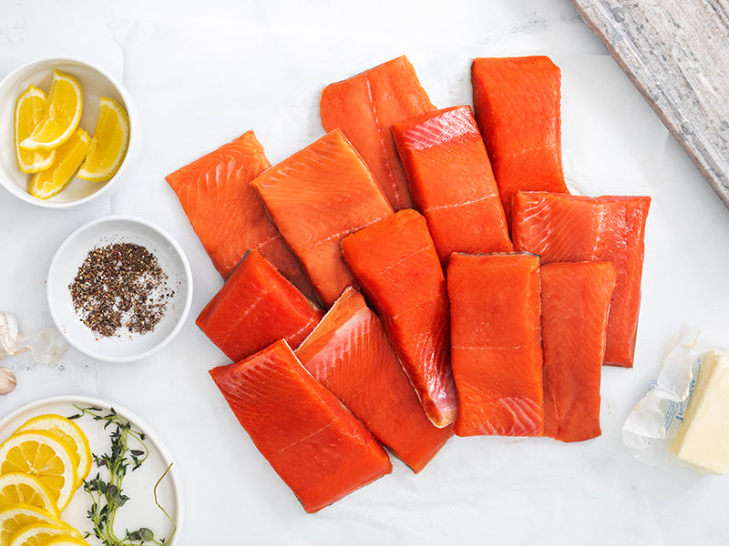 Wild Alaska Sockeye Salmon and Coho Salmon Portions on Kitchen Counter with Lemon Wedges, Seasoning, and Butter