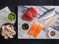 Tuna Steaks, Branzno Fillets, Atlantic Salmon Portions, and Wild Blue Shirmp on Marble Board with Herbs and Spices