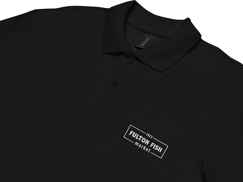 Close Up of Black Polo Shirt with White Fulton Fish Market Logo on Left Chest on White Background