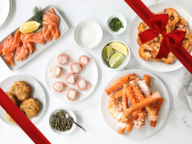 Smoked salmon, bacon-wrapped scallops, crab cakes, center cut crab legs, grilled shrimp with limes and spices on a marble table with a red bow