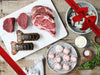 Bacon-Wrapped Scallops, Shrimp, Lobster Tails, Filet Mignon, and Ribeye Steak on Plates on Wood Table with Gift Bow Graphic