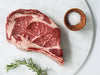 Raw Pat LaFrieda Dry Aged Ribeye Bone-In Steak with Salt and Rosemary on a Marble Surface
