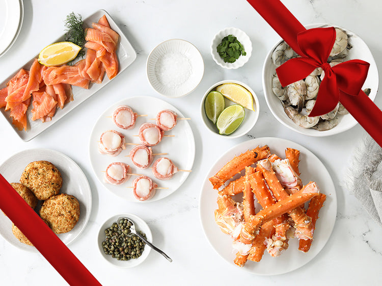 Crab Cakes, Crab Legs, Smoked Salmon, Bacon-Wrapped Scallops, and Shrimp on Plates on Table with Gift Bow Graphic