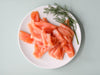 Signature Smoked Salmon pieces on a white plate with dill on a light blue background