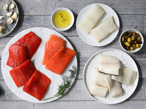Wild Alaska Sockeye and Coho Salmon Portions, Wild Alaska Pacific Halibut Portions, and Wild Alaska Black Cod Portions on Plates on Wood Table