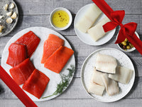 Wild Alaska Copper River Sockeye Salmon, Coho Salmon, Pacific Halibut, and Black Cod Portions on Plates on Wood Table with Gift Bow Graphic